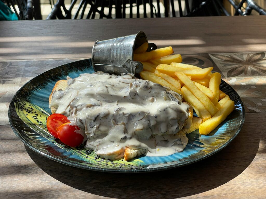 Close-up of a delicious mushroom toast with cream sauce and fries on a vibrant platter.